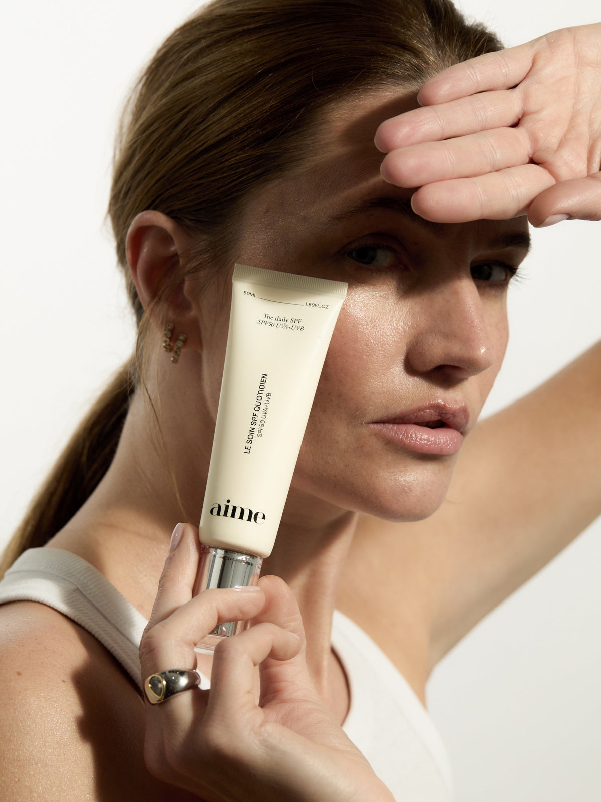 AIME The Daily SPF SPF50 UVA+UVB sunscreen held by a model
