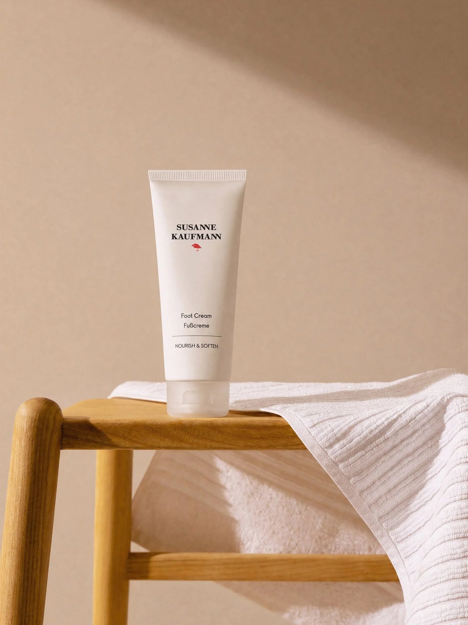 A Tube of SUSANNE KAUFMANN Foot Cream standing on a wooden stool with a white towel draped over it