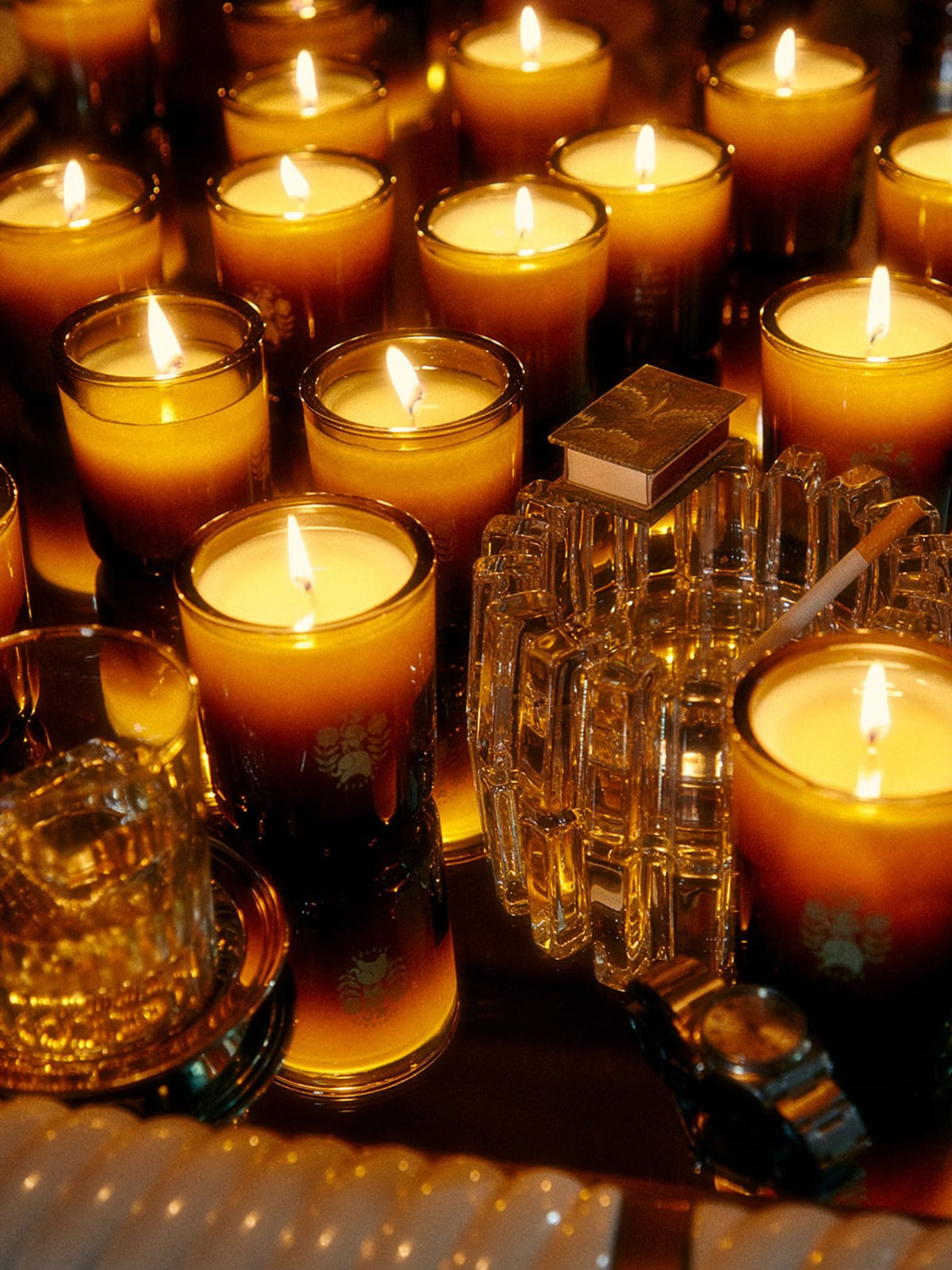 Flamingo Estate Adriatic Muscatel Sage Candle surrounded by glowing candles and glass fragrance bottles