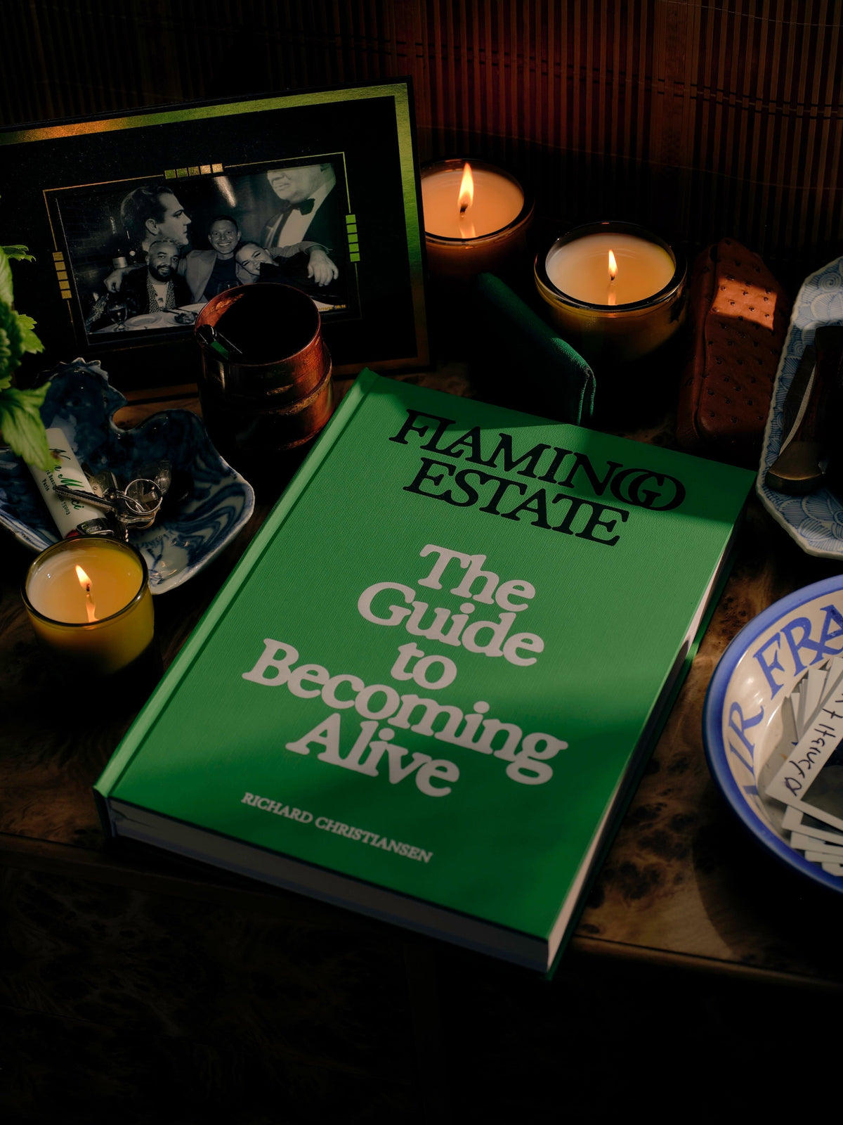 Flamingo Estate The Guide to Becoming Alive book displayed on a table with lit candles and decorative objects