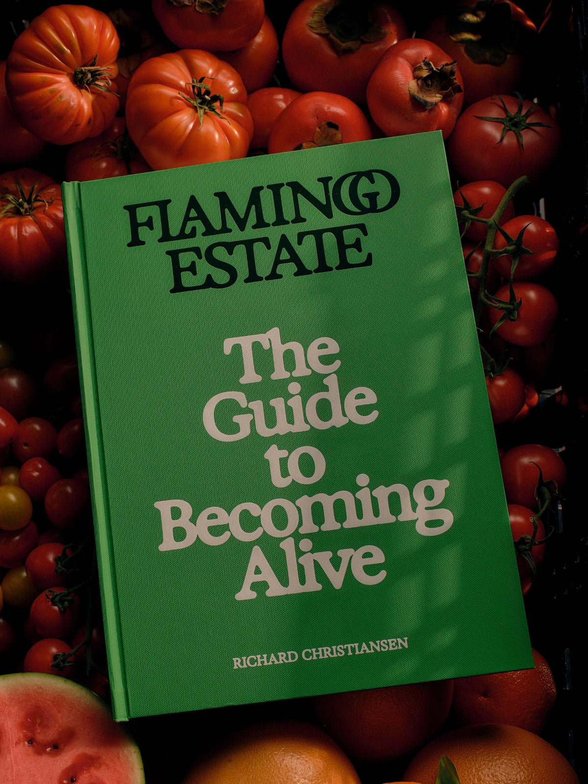 Flamingo Estate The Guide to Becoming Alive by Richard Christiansen displayed among fresh tomatoes