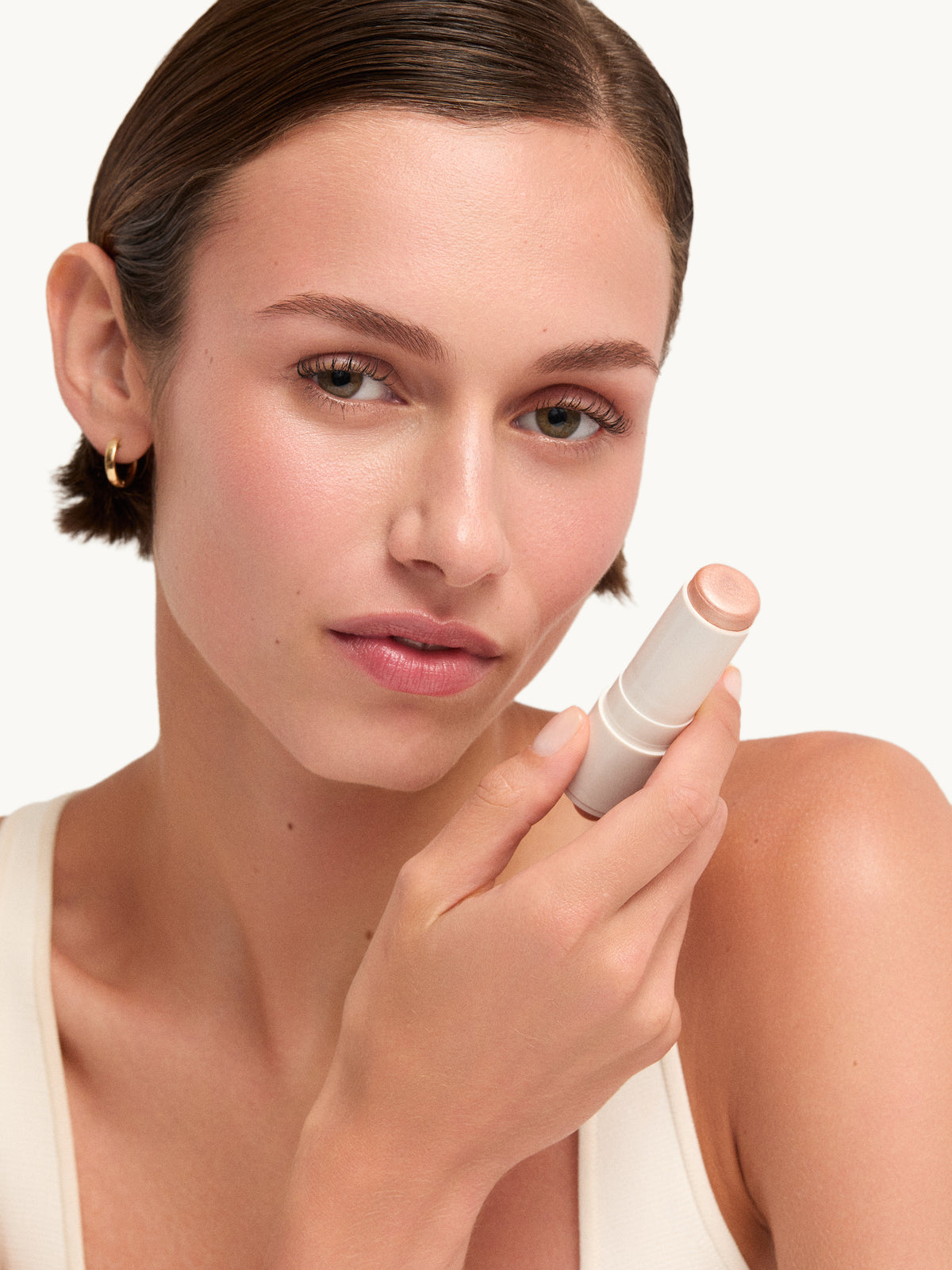 Model holding goop beauty Glow Skin Highlighter Stick in Aura