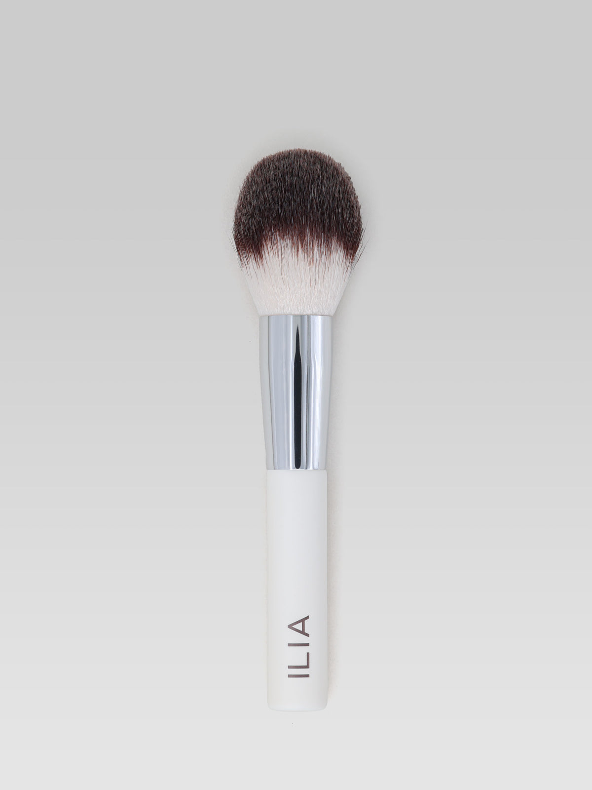 ILIA BEAUTY Finishing Powder Brush with soft, fluffy bristles, a silver ferrule and a white handle for applying finishing powder.