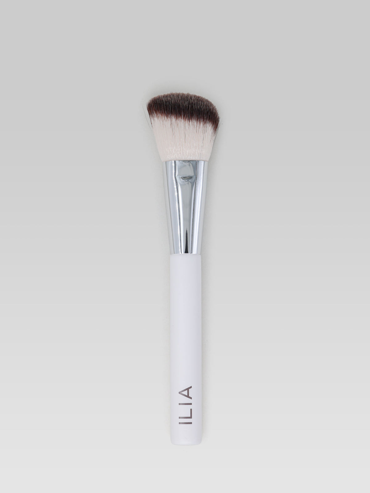 ILIA BEAUTY Sculpting Brush with angled, dense bristles, a silver ferrule and a white handle for precise makeup application and sculpting.