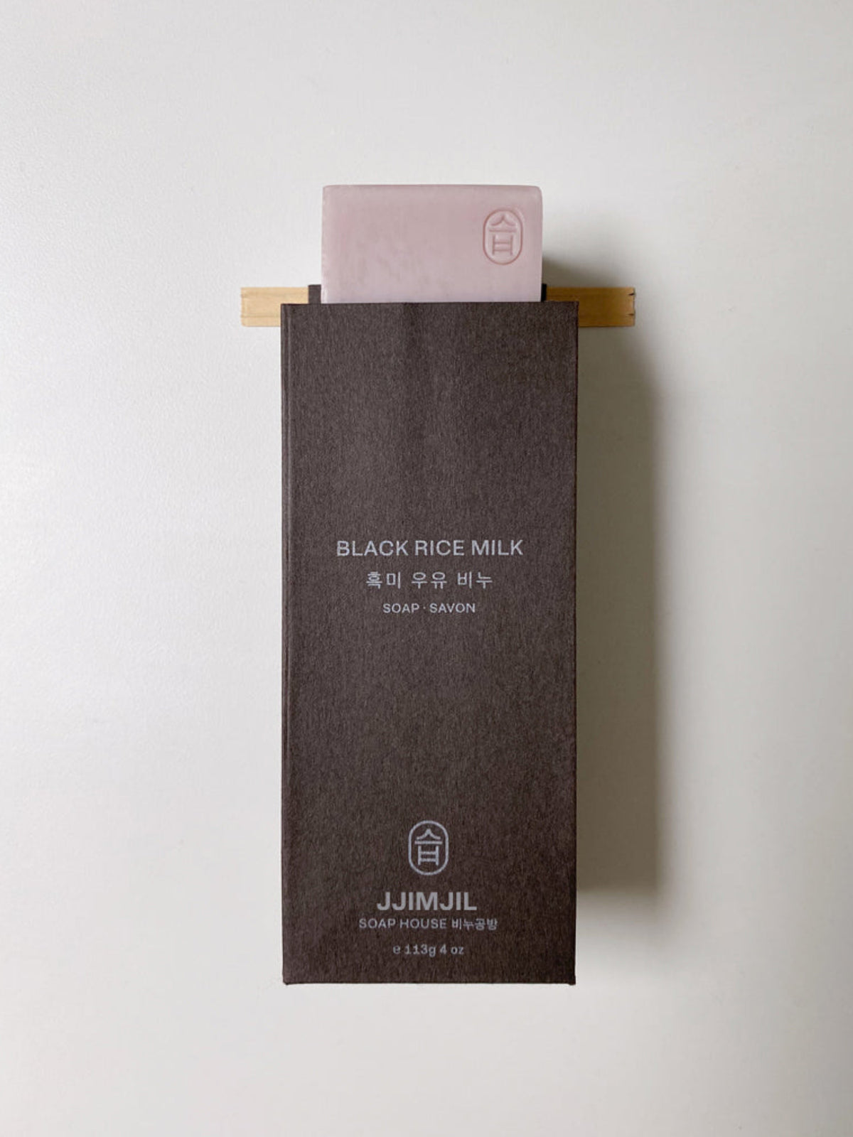 Jjimjil Black Rice Milk Soap bar in dark brown packaging with a pink soap bar, displayed against a clean white background.