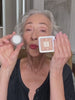 RMS Beauty founder Rose-Marie Swift comparing the Living Luminizer with another highlighter, demonstrating the products on camera