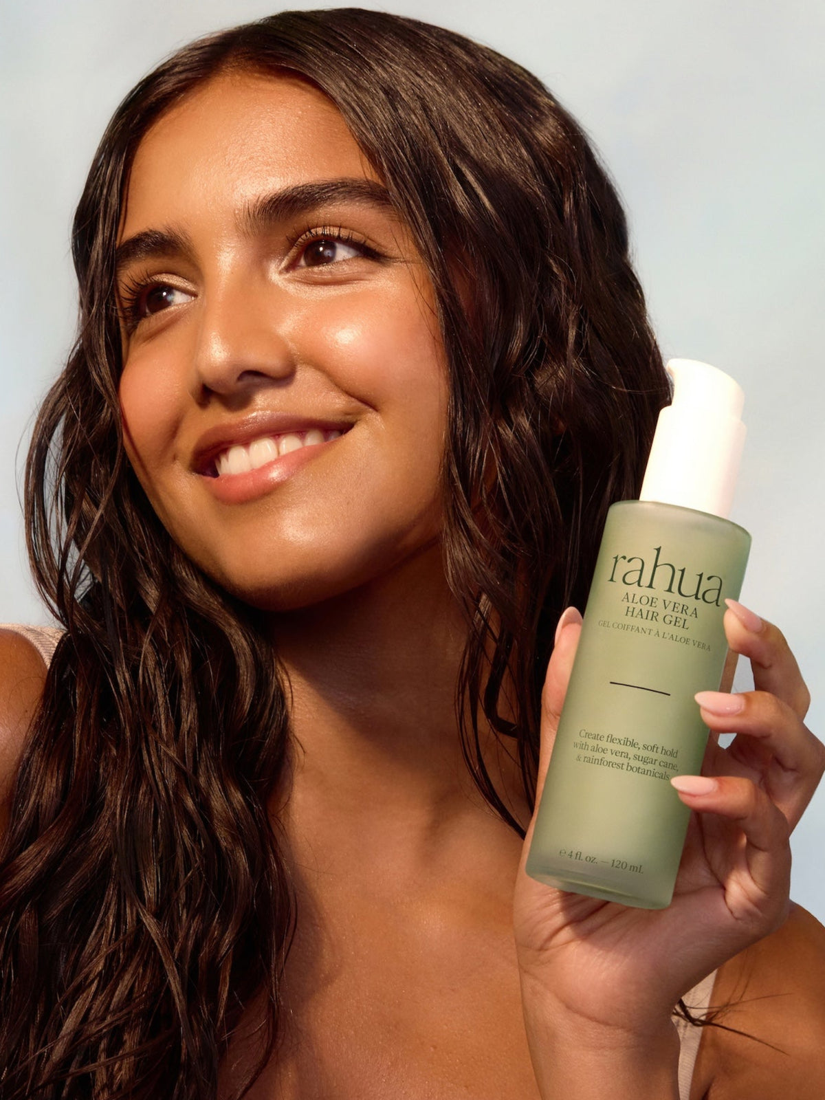 Woman holding Rahua Aloe Vera Hair Gel with long, defined wavy hair