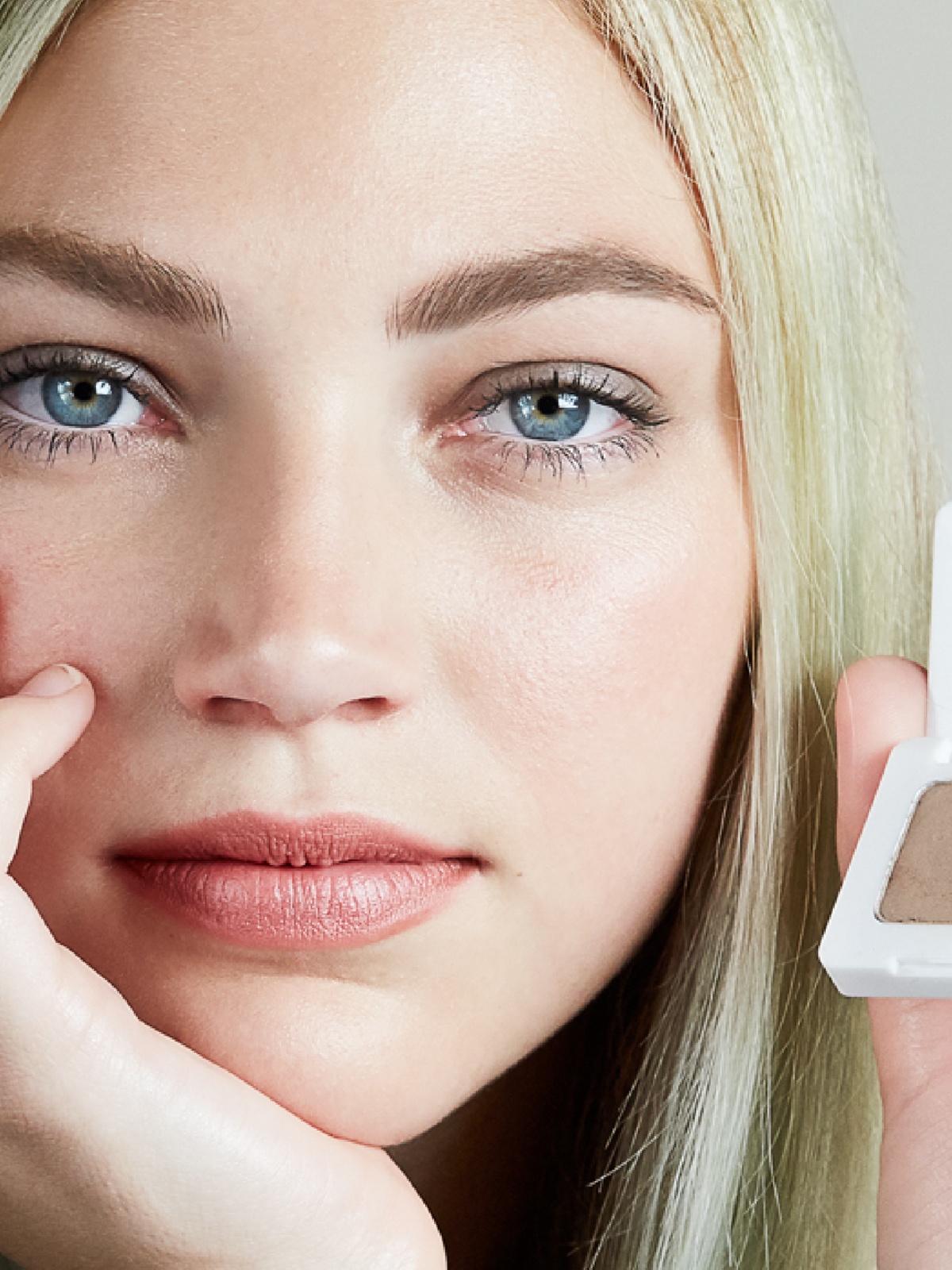 Close-up of a blonde model holding RMS Beauty Back2Brow Powder in Light beside her face