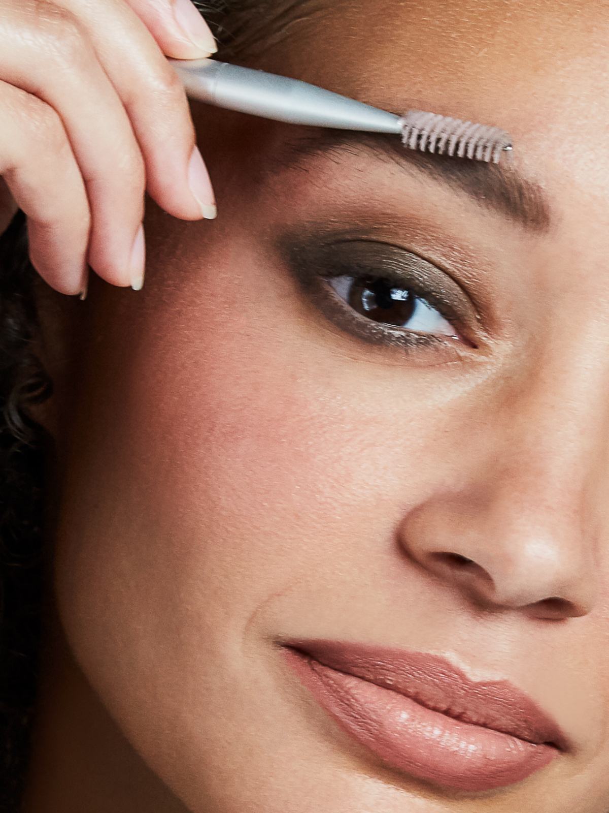 Close-up of a brunette model grooming her eyebrows with a spoolie brush
