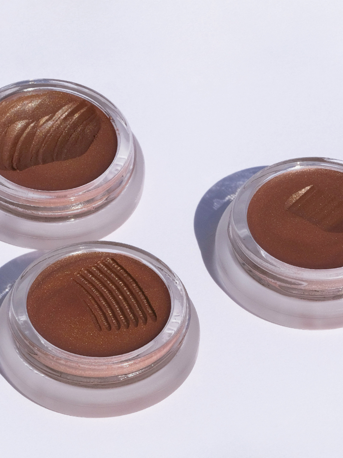 Three open RMS Beauty Buriti Cream Bronzer pots showing the creamy formula and textured product surface