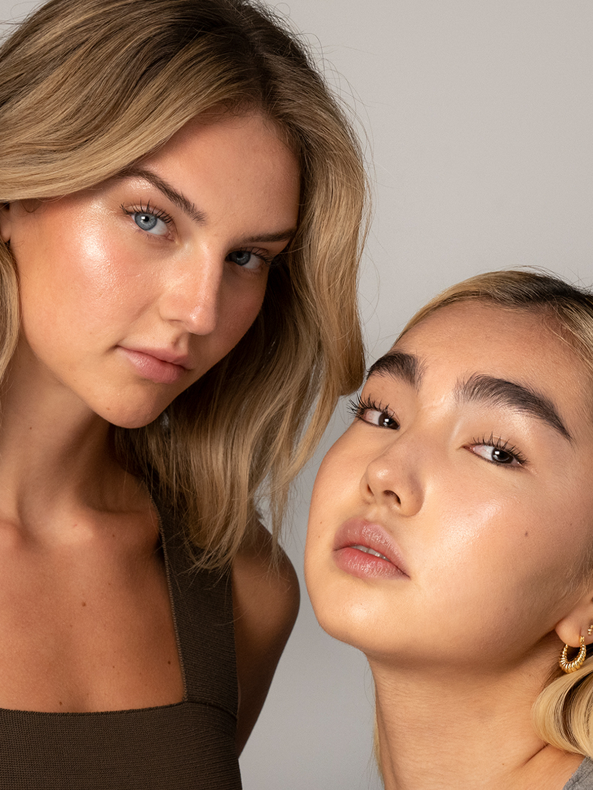 Two models wearing RMS Beauty Champagne Rosé Luminizer, showcasing radiant, luminous skin with a champagne-pink highlight on the cheekbones