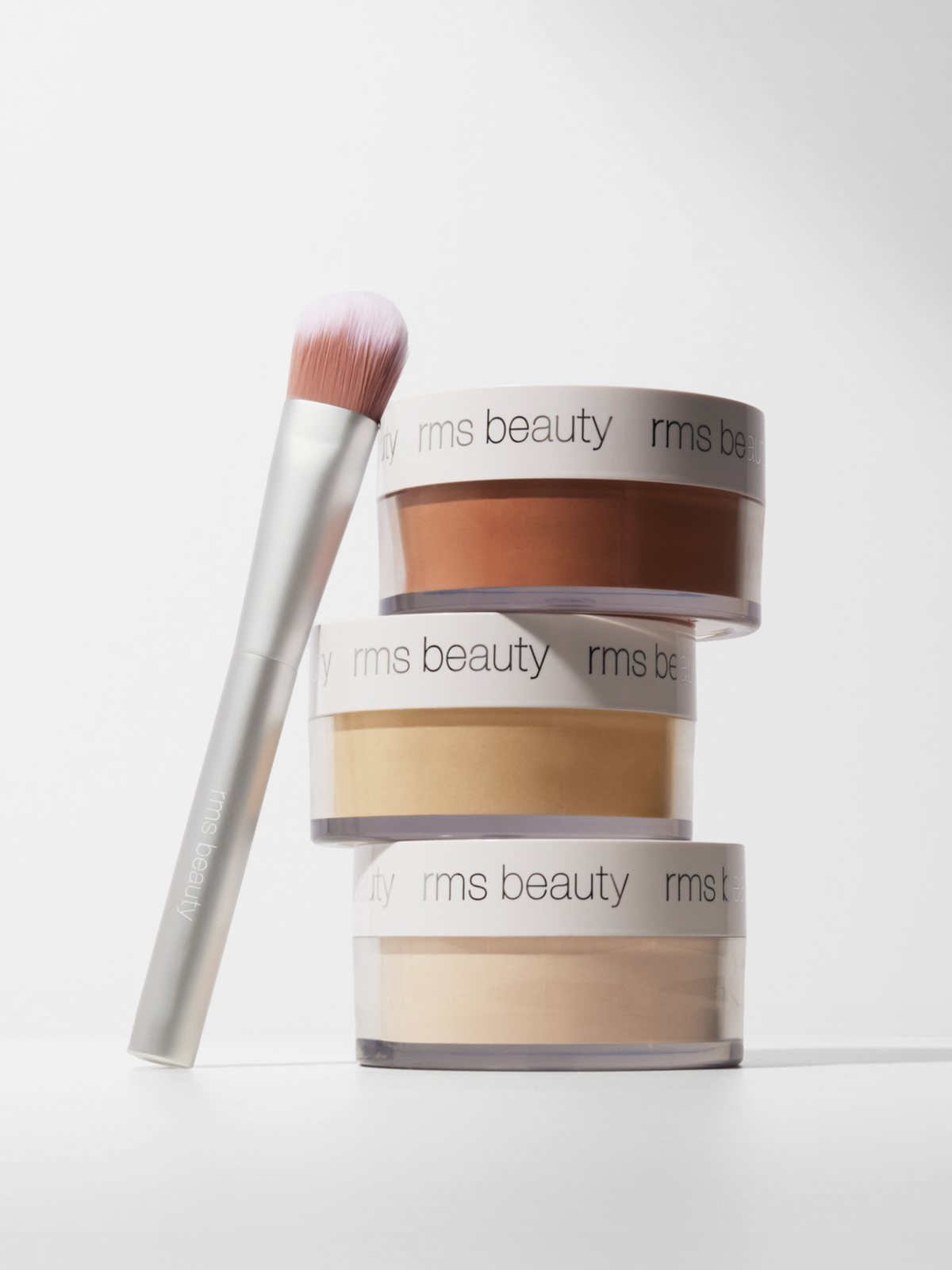 RMS Beauty Hydra Setting Powder in multiple shades with a makeup brush