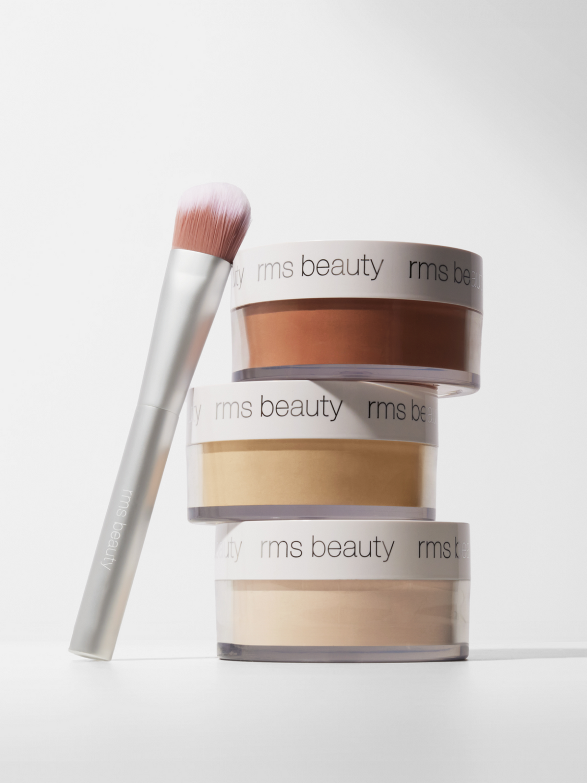 RMS Beauty Hydra Setting Powder in three shades displayed with a makeup brush