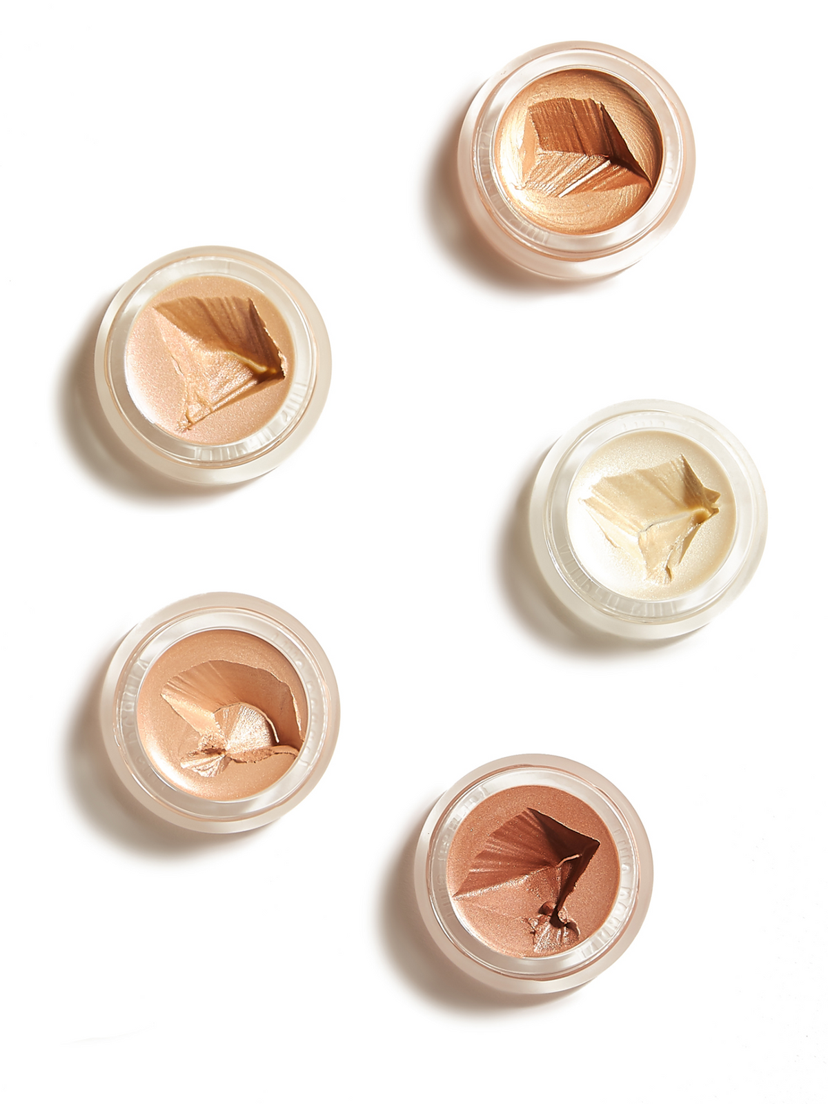 Five RMS Beauty luminizers in open round pots, showcasing a range of champagne, golden, peach and bronze highlighting shades on a white background