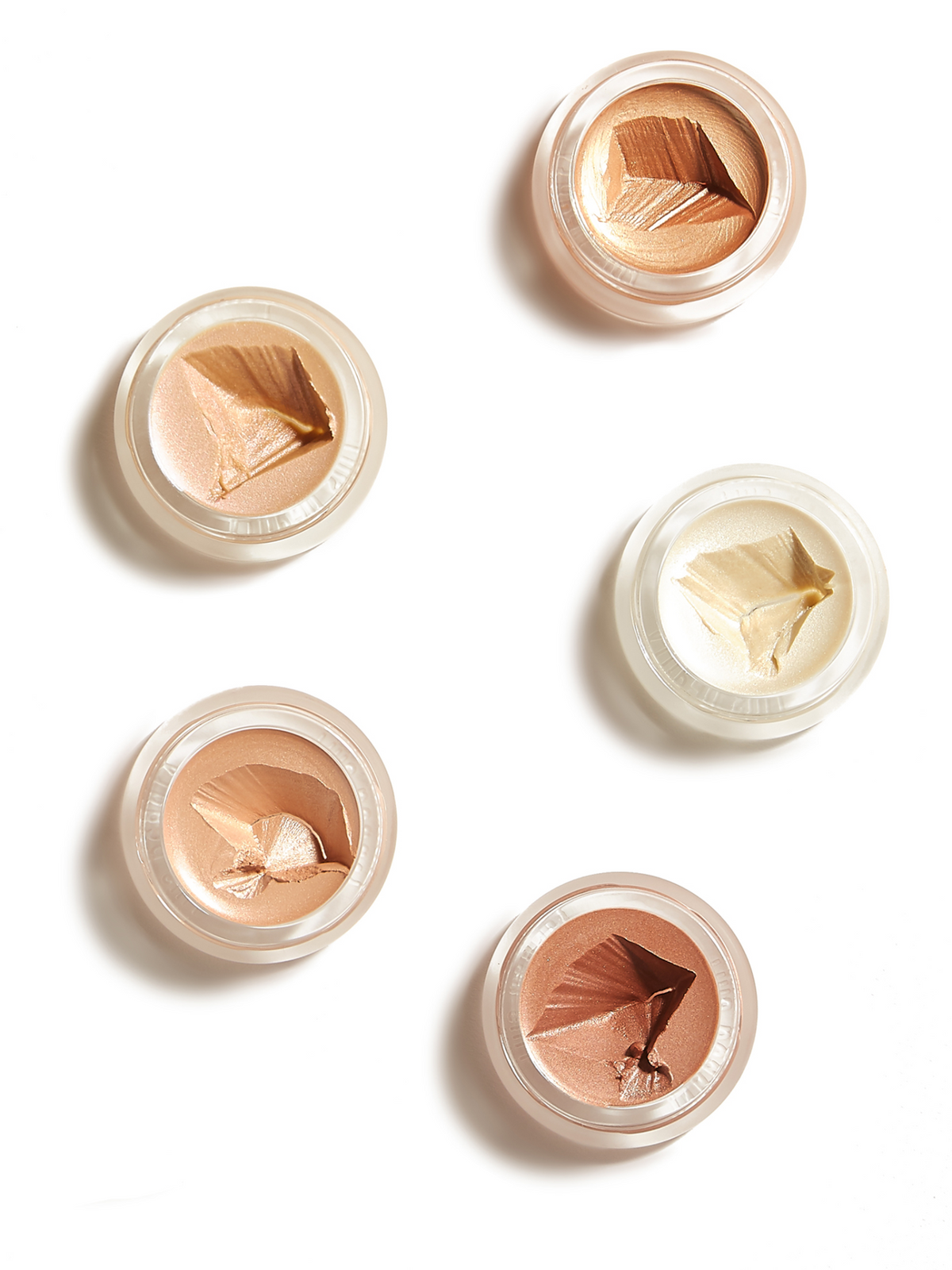 Five RMS Beauty luminizers in open round pots, showcasing a range of champagne, golden, peach and bronze highlighting shades on a white background