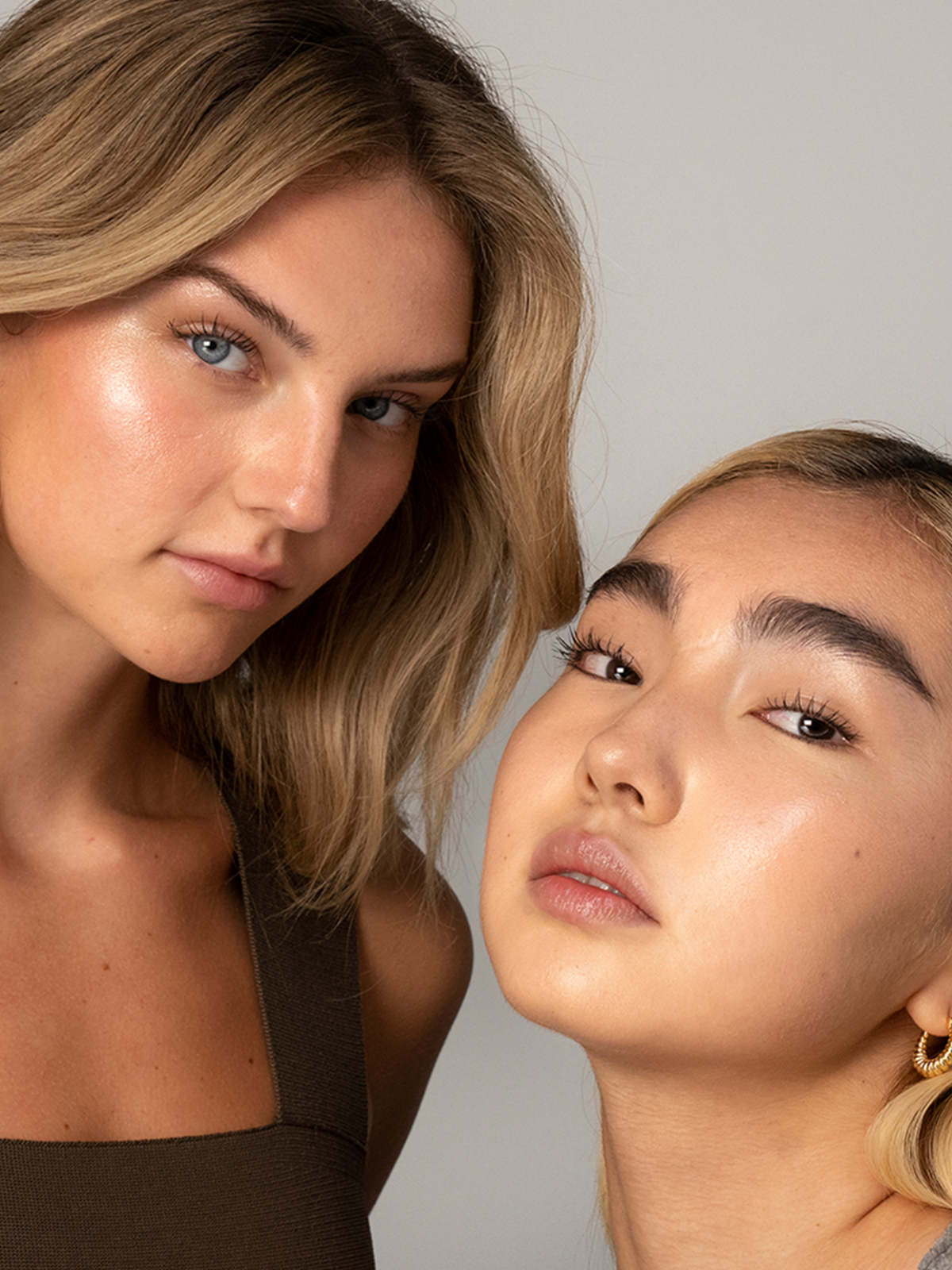 Two models wearing RMS Beauty Magic Luminizer, showcasing radiant, dewy skin with a luminous champagne-peach glow on the cheekbones