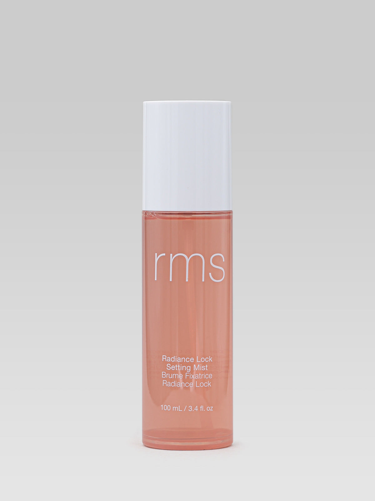 RMS Beauty Radiance Lock Setting Mist 100 ml in a translucent peach bottle with a white cap against a light grey background