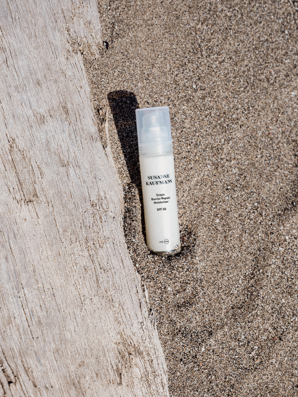 SUSANNE KAUFMANN Ectoin Barrier Repair Day Moisturiser SPF 50 bottle on a sandy surface beside weathered wood