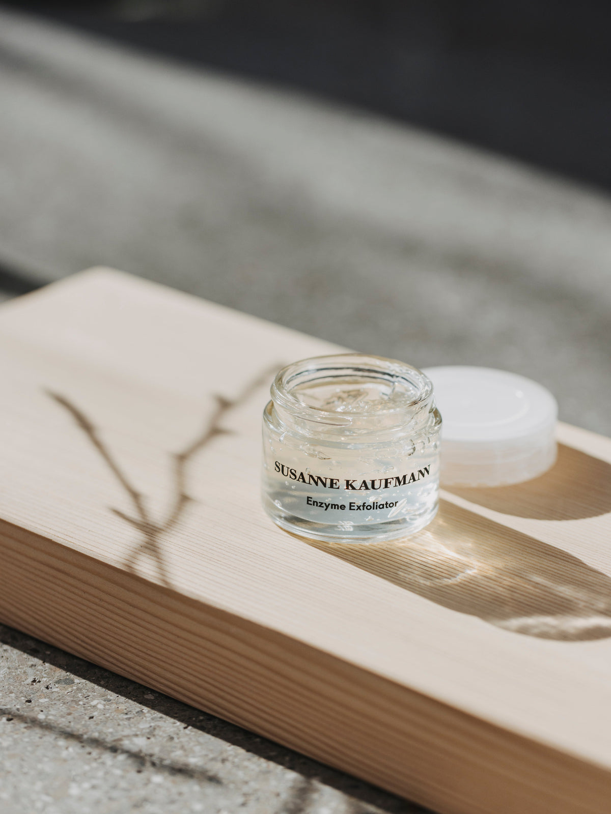 Open jar of Susanne Kaufmann Enzyme Exfoliator on a wooden surface in natural sunlight
