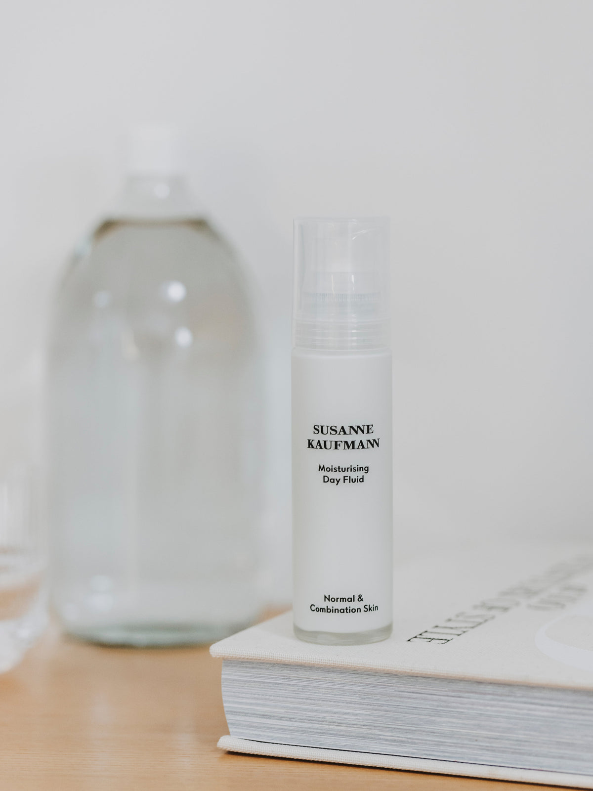 Susanne Kaufmann Moisturising Day Fluid displayed beside a glass bottle and a book on a wooden surface
