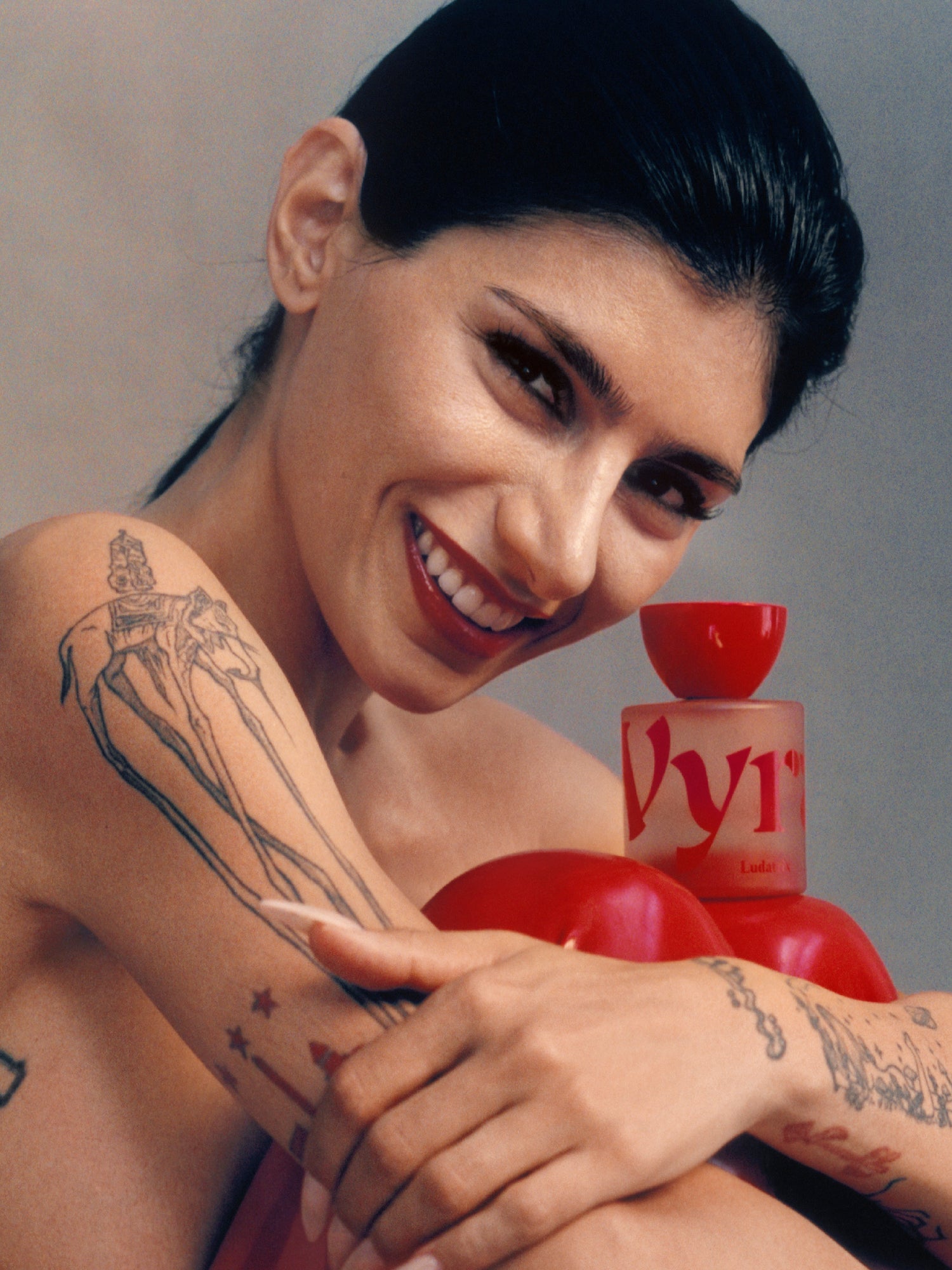 VYRAO Ludatrix Eau de Parfum bottle held by a smiling woman surrounded by red objects