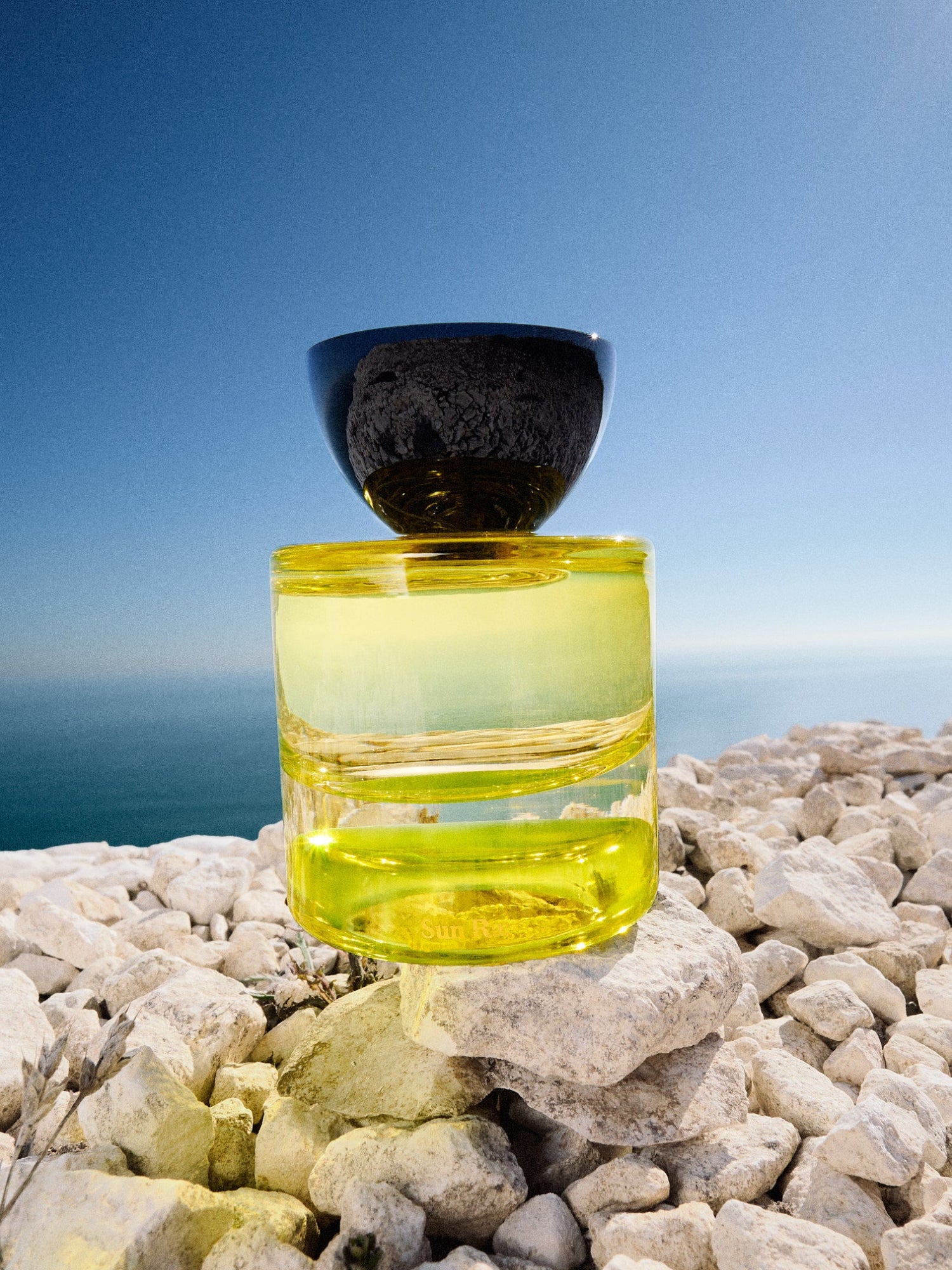 VYRAO Sun Rae Eau de Parfum bottle on rocks against a blue sky